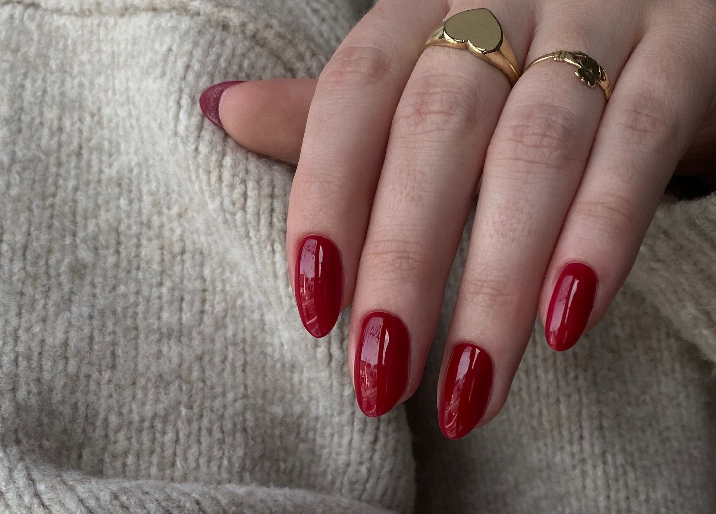 Elegant red manicured nails at Kristina.NailStudio in Naas, County Kildare, IE, displayed against a textured sweater.