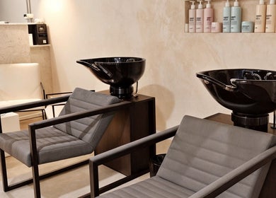 Área de lavado en ATICA Salón, Madrid, Comunidad De Madrid, ES, mostrando sillas modernas y lavabos negros.