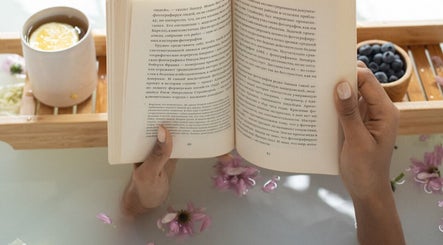 Hands holding a book over a serene bath with a cup at Get Me Pampered (London), London, England, GB.