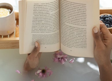 Hands holding book in a bath with flowers at Get Me Pampered (Llandudno), Llandudno, GB.