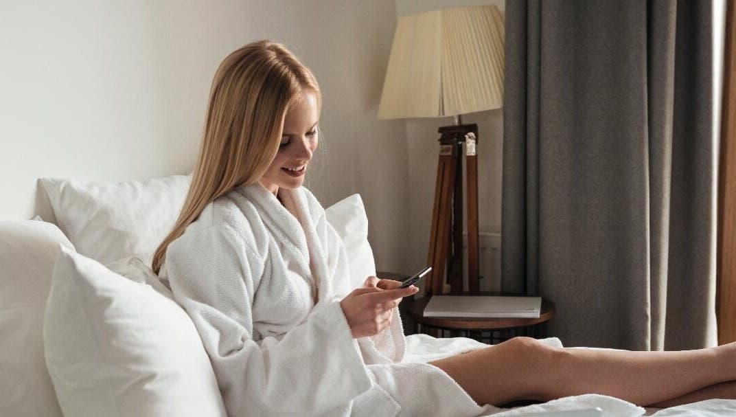 Woman in bathrobe relaxing, checking phone, at Get Me Pampered (Falkirk), Falkirk, GB.