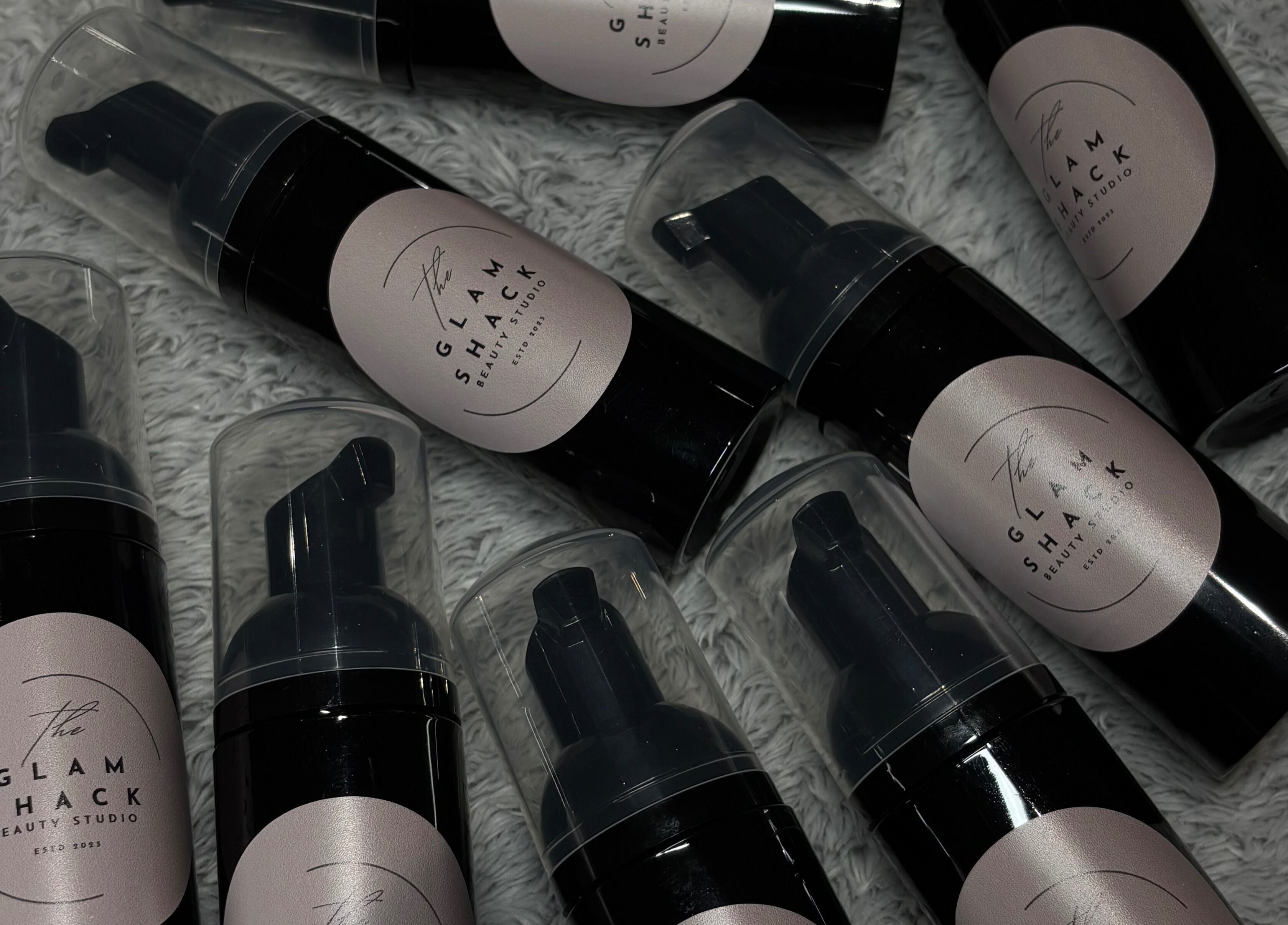 Luxury beauty foam bottles from The Glam Shack, Mawsley, England, GB, displayed on a textured surface.