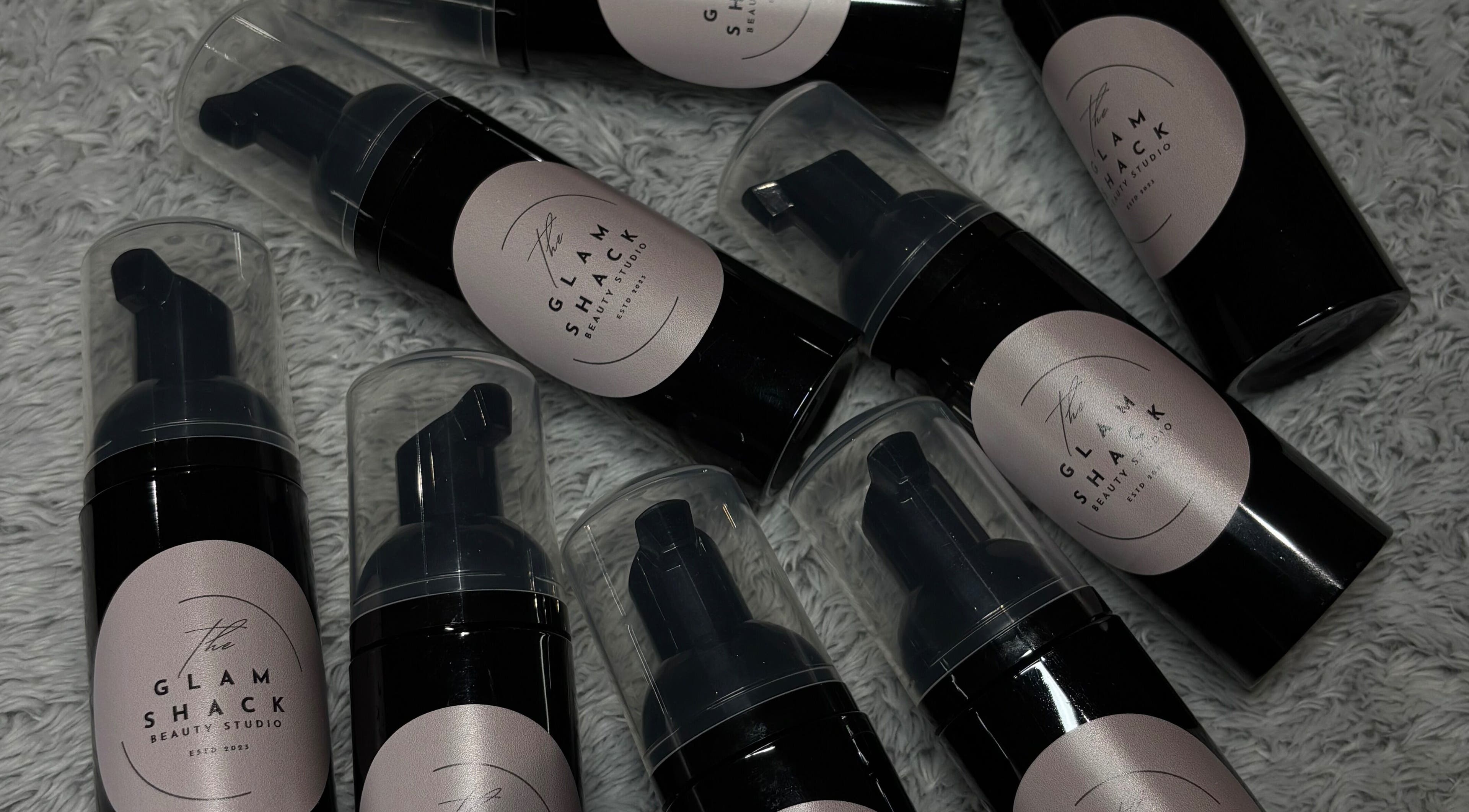 Luxury beauty foam bottles from The Glam Shack, Mawsley, England, GB, displayed on a textured surface.