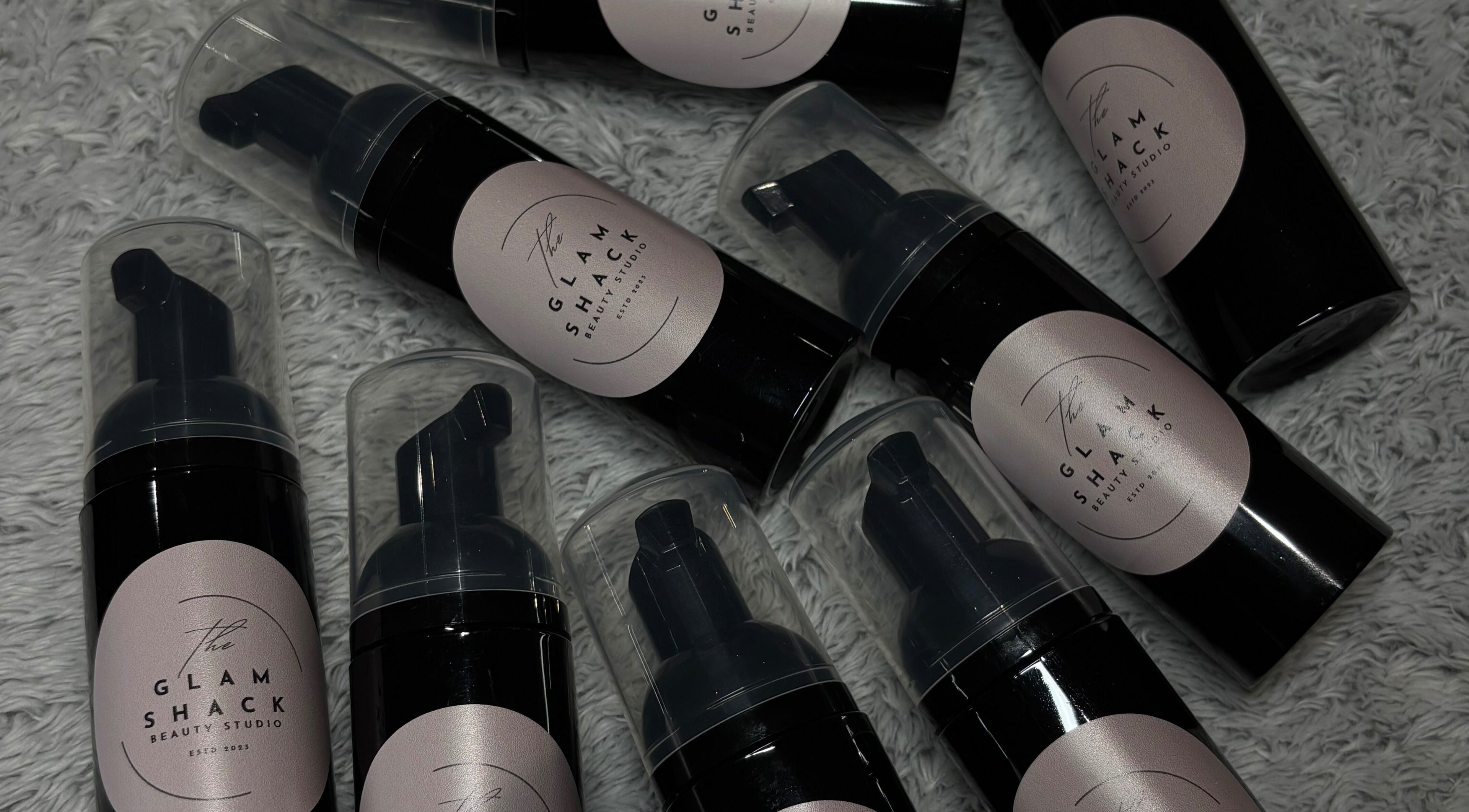 Luxury beauty foam bottles from The Glam Shack, Mawsley, England, GB, displayed on a textured surface.