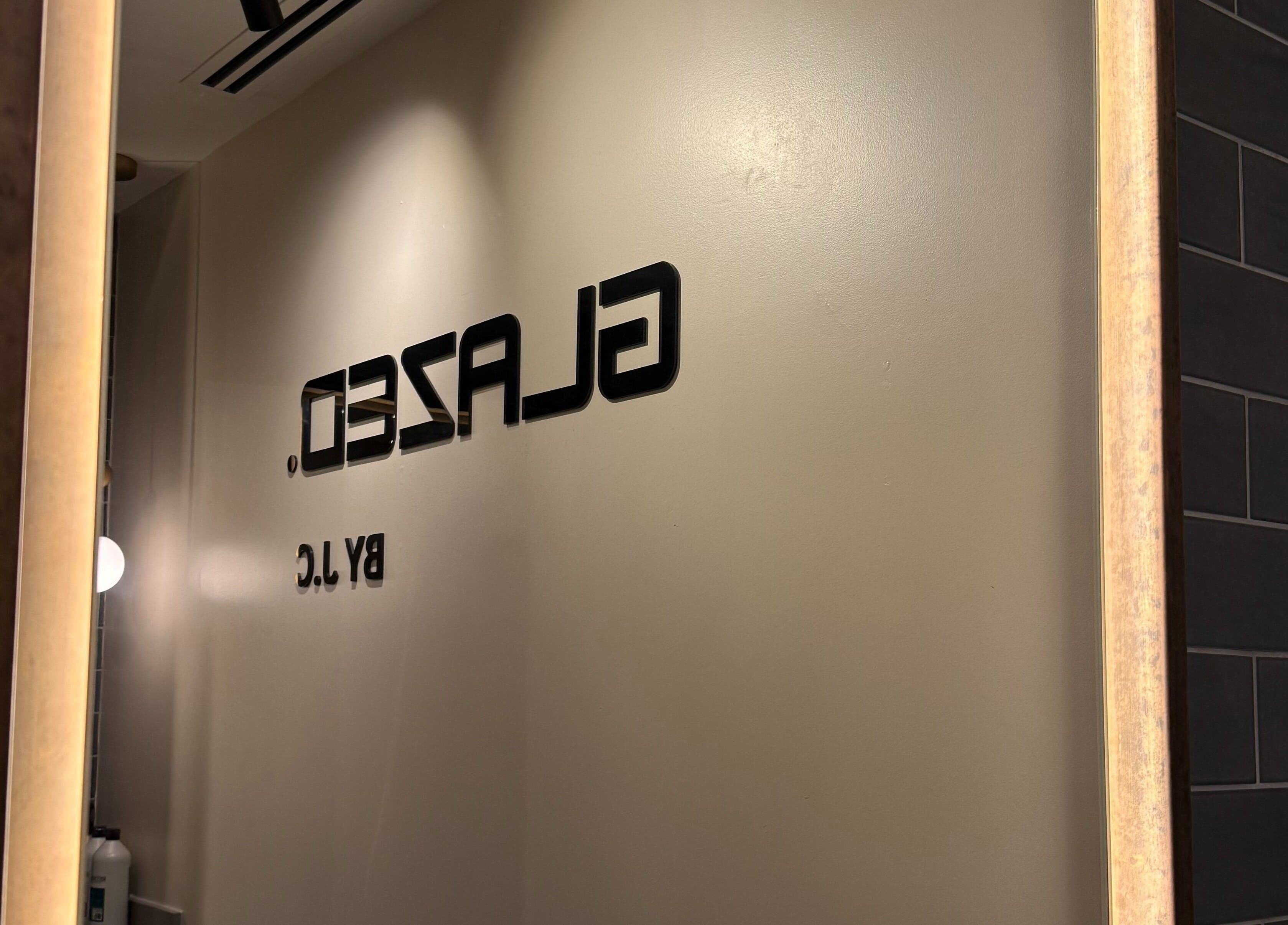 Elegant wall signage of GLAZED By JC in Mottram, England, GB seen through a stylish mirror.