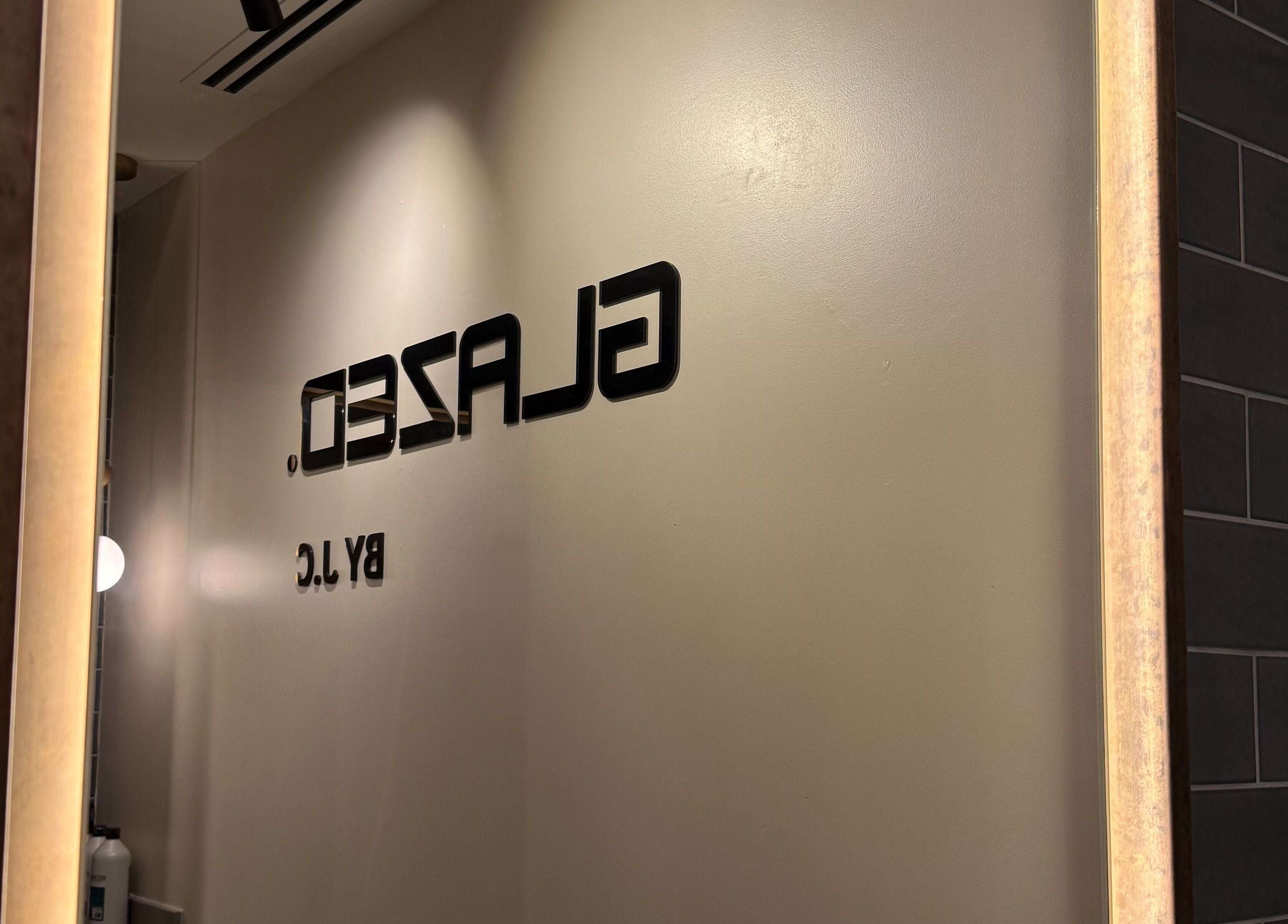 Elegant wall signage of GLAZED By JC in Mottram, England, GB seen through a stylish mirror.