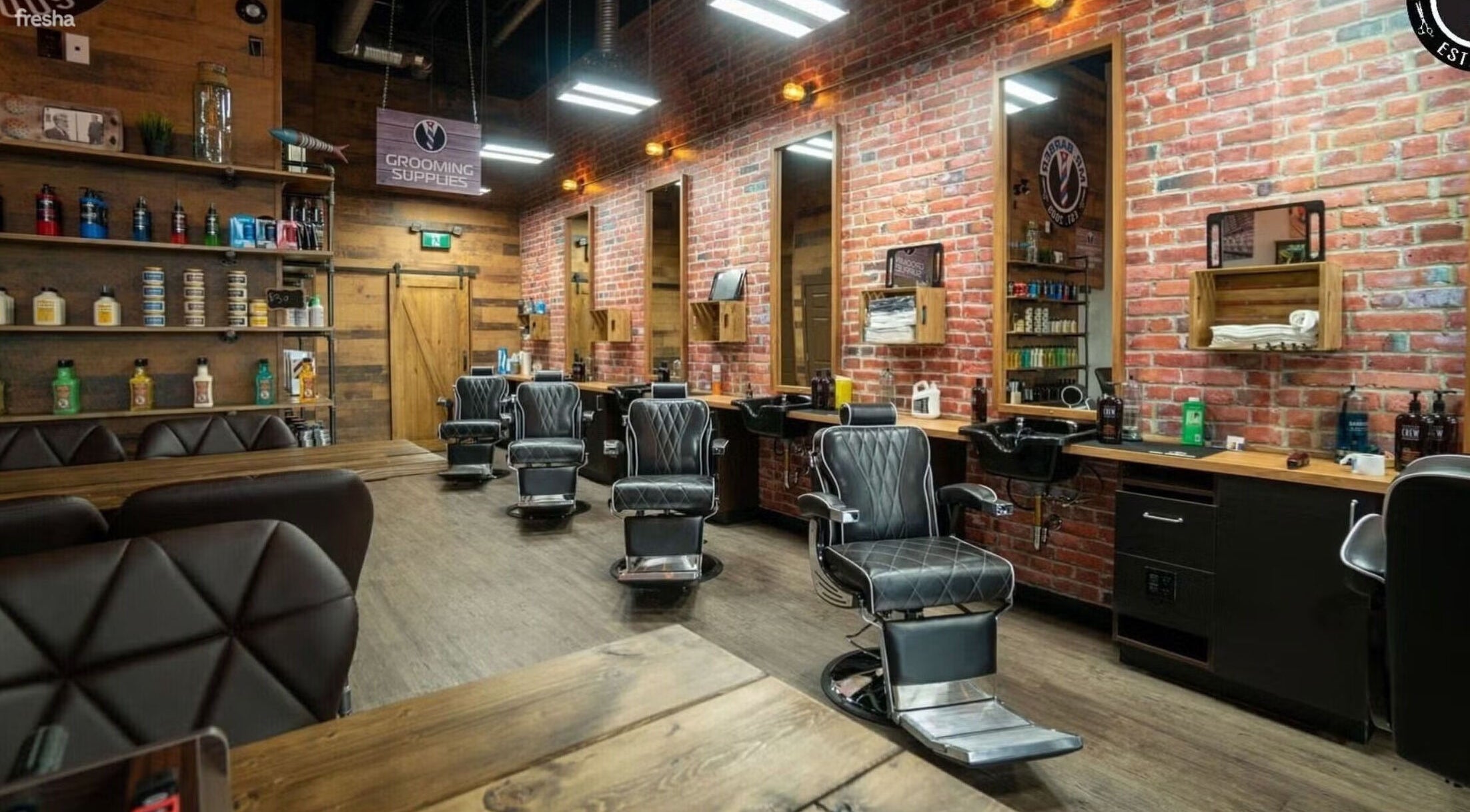 Interior of Mr. Barber Tamarack in Edmonton, Alberta, CA featuring sleek black barber chairs and brick wall decor.