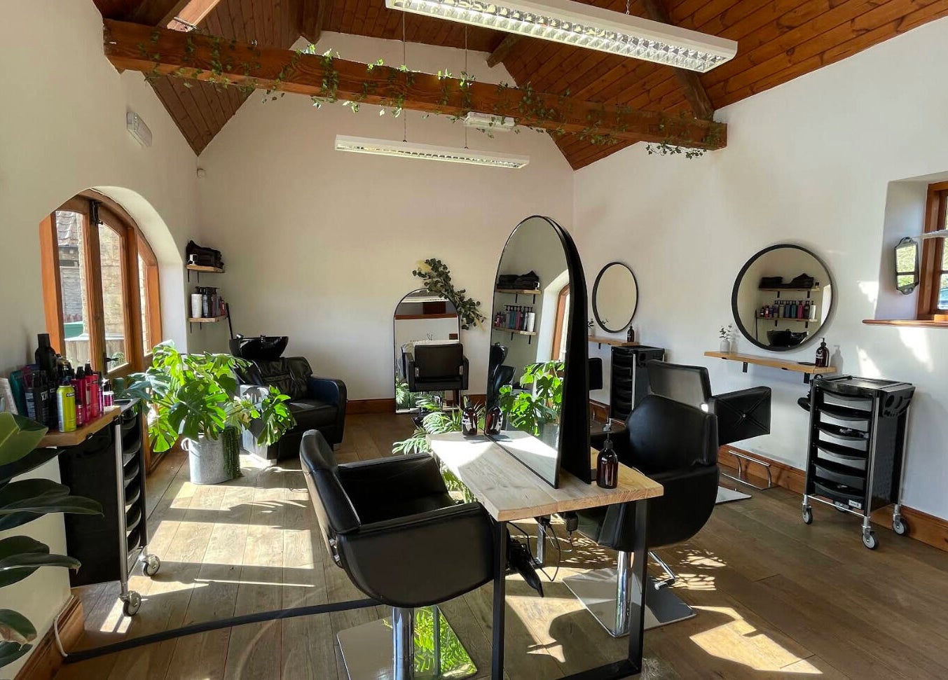 Bright and modern salon interior at Bavaro in Aldwincle, England, GB with stylish black chairs and mirrors.