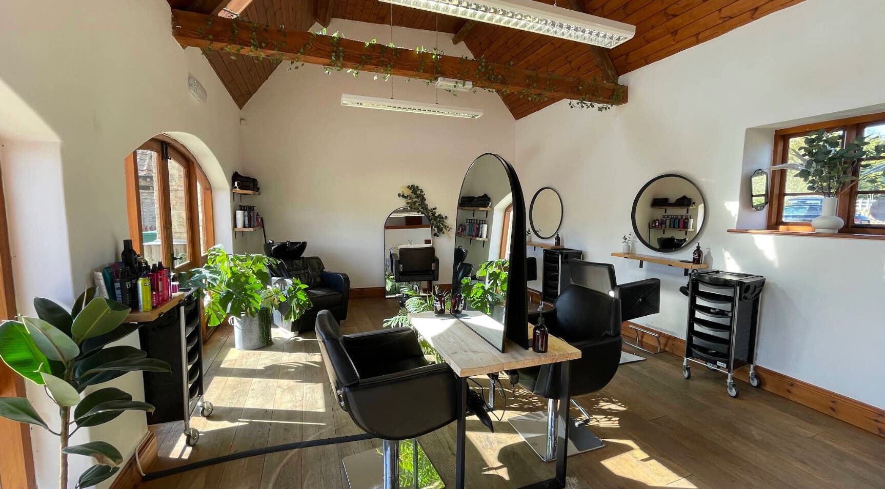 Bright and modern salon interior at Bavaro in Aldwincle, England, GB with stylish black chairs and mirrors.