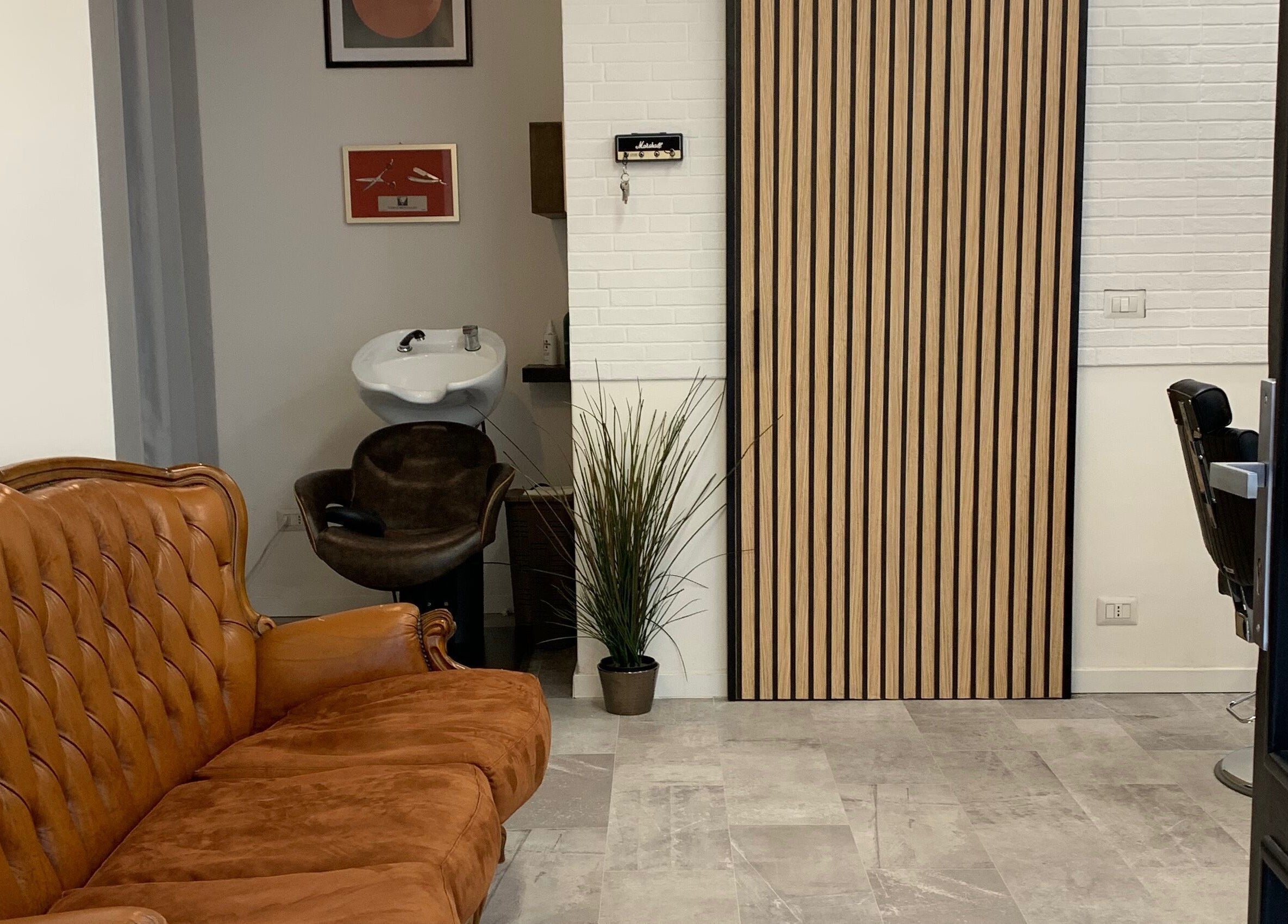 Interno accogliente di Verve Men Salon, Selargius, Sardegna, IT con divano in pelle e lavandino moderno.