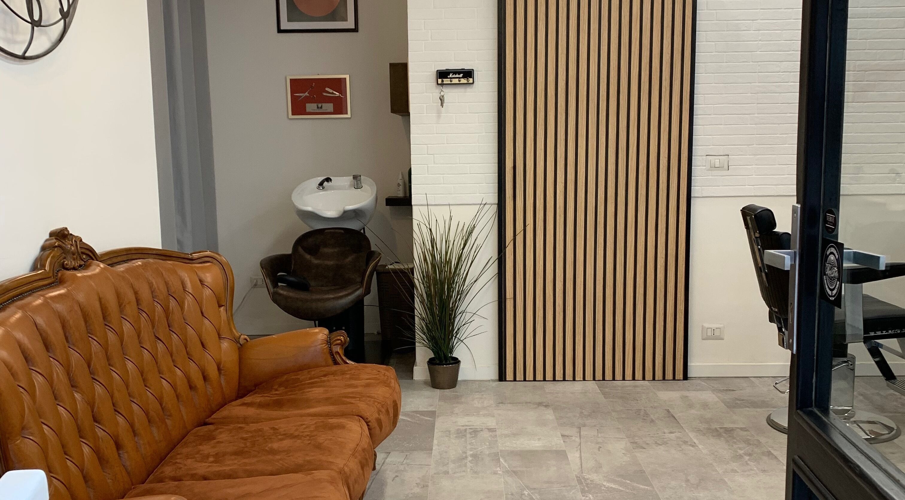 Interno accogliente di Verve Men Salon, Selargius, Sardegna, IT con divano in pelle e lavandino moderno.