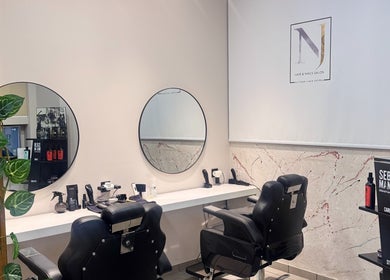 Κομψός χώρος κουρέματος στο NJ HAIR & NAILS SALON, Νέα Σμύρνη, GR. Δύο μαύρες καρέκλες μπροστά από καθρέφτες.