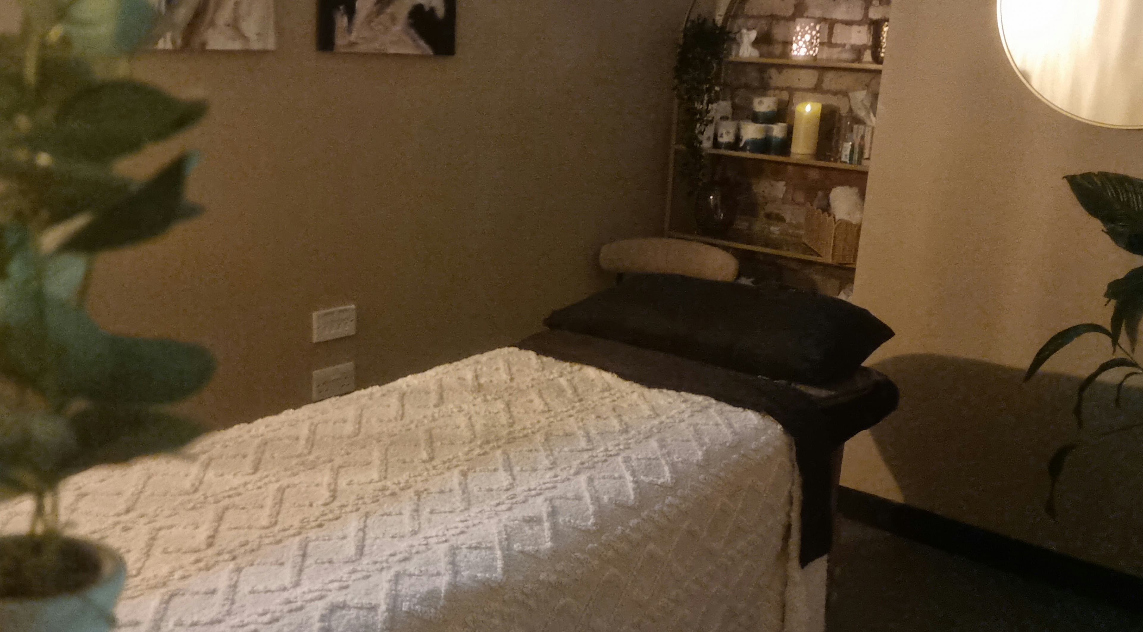 Cozy massage room at Bee Revived, with a soft bed, plants, and warm lighting in Manchester, England, GB.