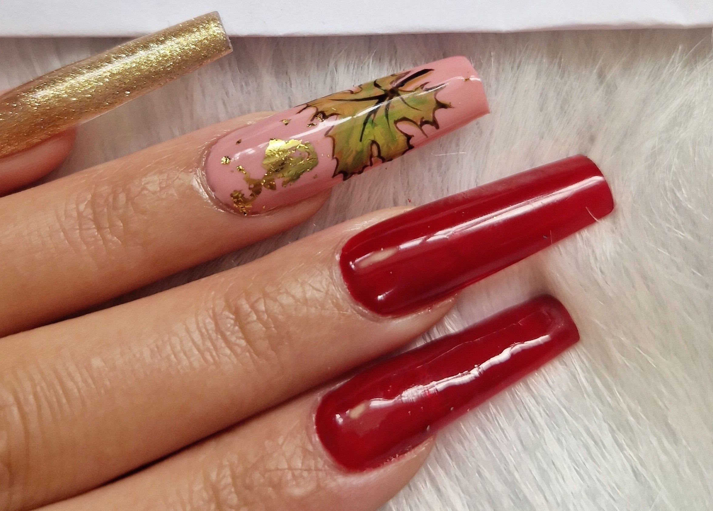Intricate nail art with gold leaf and red tones at Fantasy Nails, Holyhead, Cymru, GB.