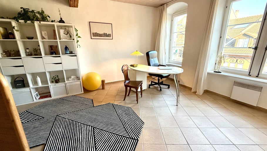 Bureau lumineux au MTC Eglantine, Morges, Vaud, CH. Intérieur avec fauteuil, table, étagères blanches.