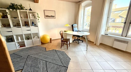 Bureau lumineux au MTC Eglantine, Morges, Vaud, CH. Intérieur avec fauteuil, table, étagères blanches.