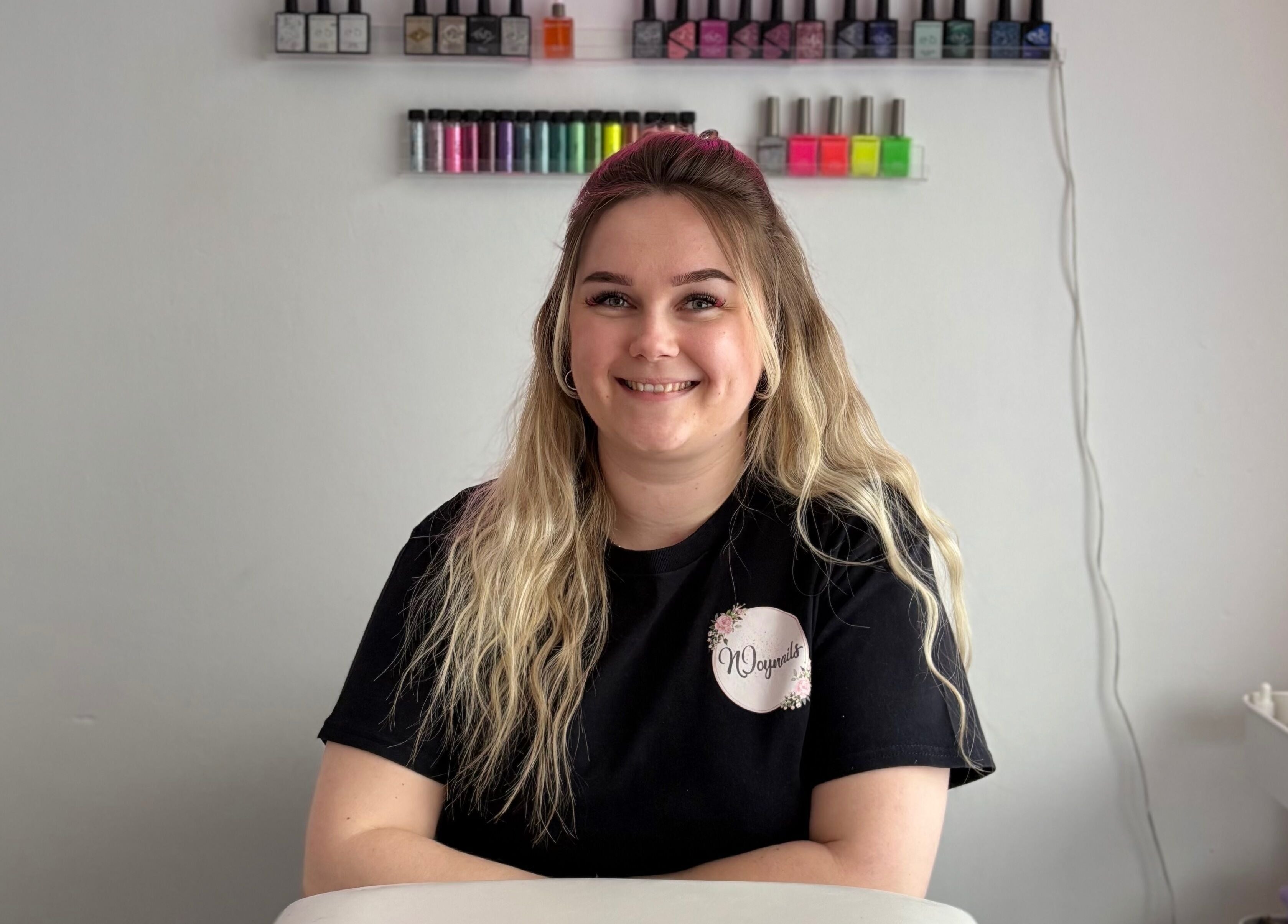 Smiling staff at Njoynails, Stanbridge, England, GB, showcasing vibrant nail polish selection.