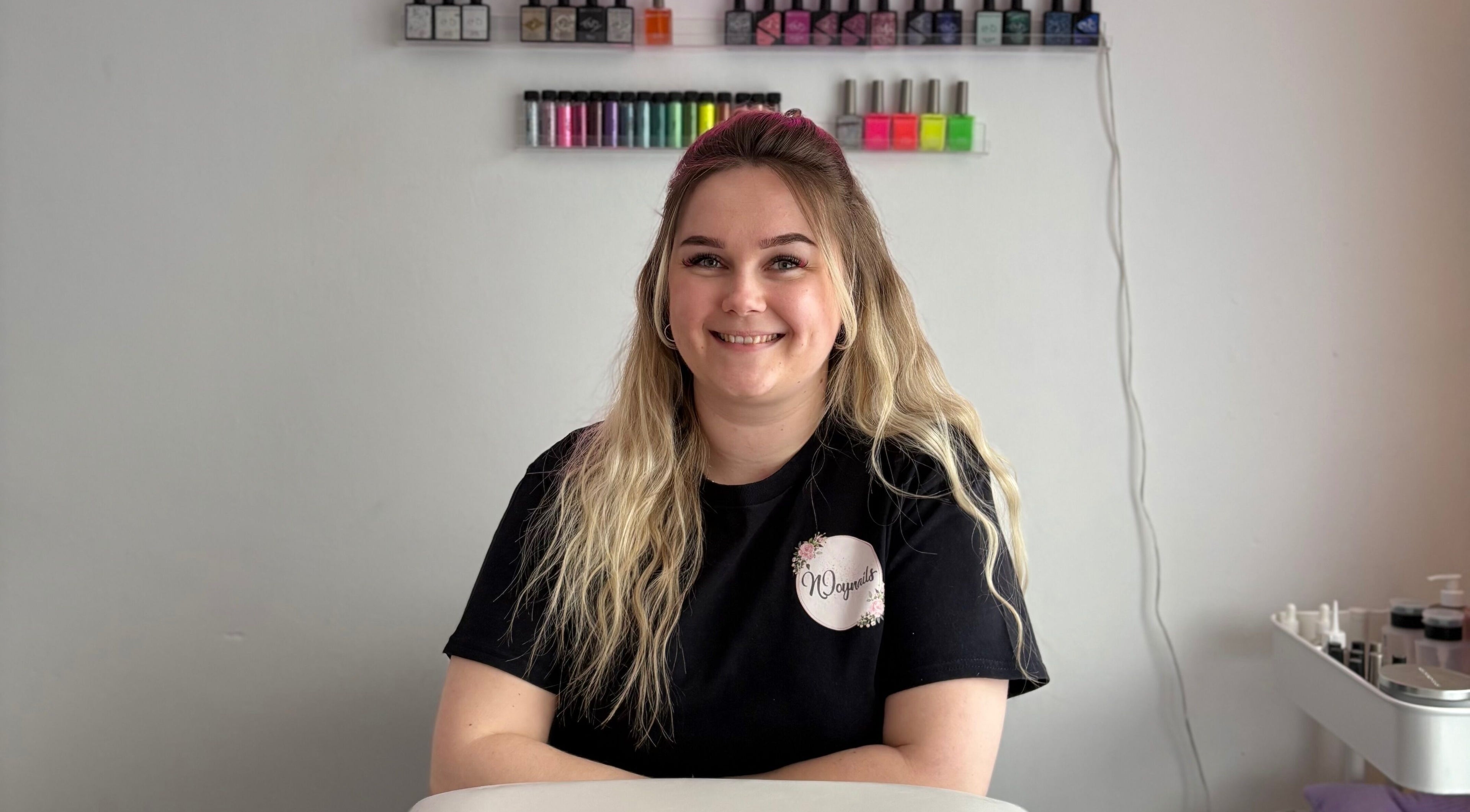 Smiling staff at Njoynails, Stanbridge, England, GB, showcasing vibrant nail polish selection.