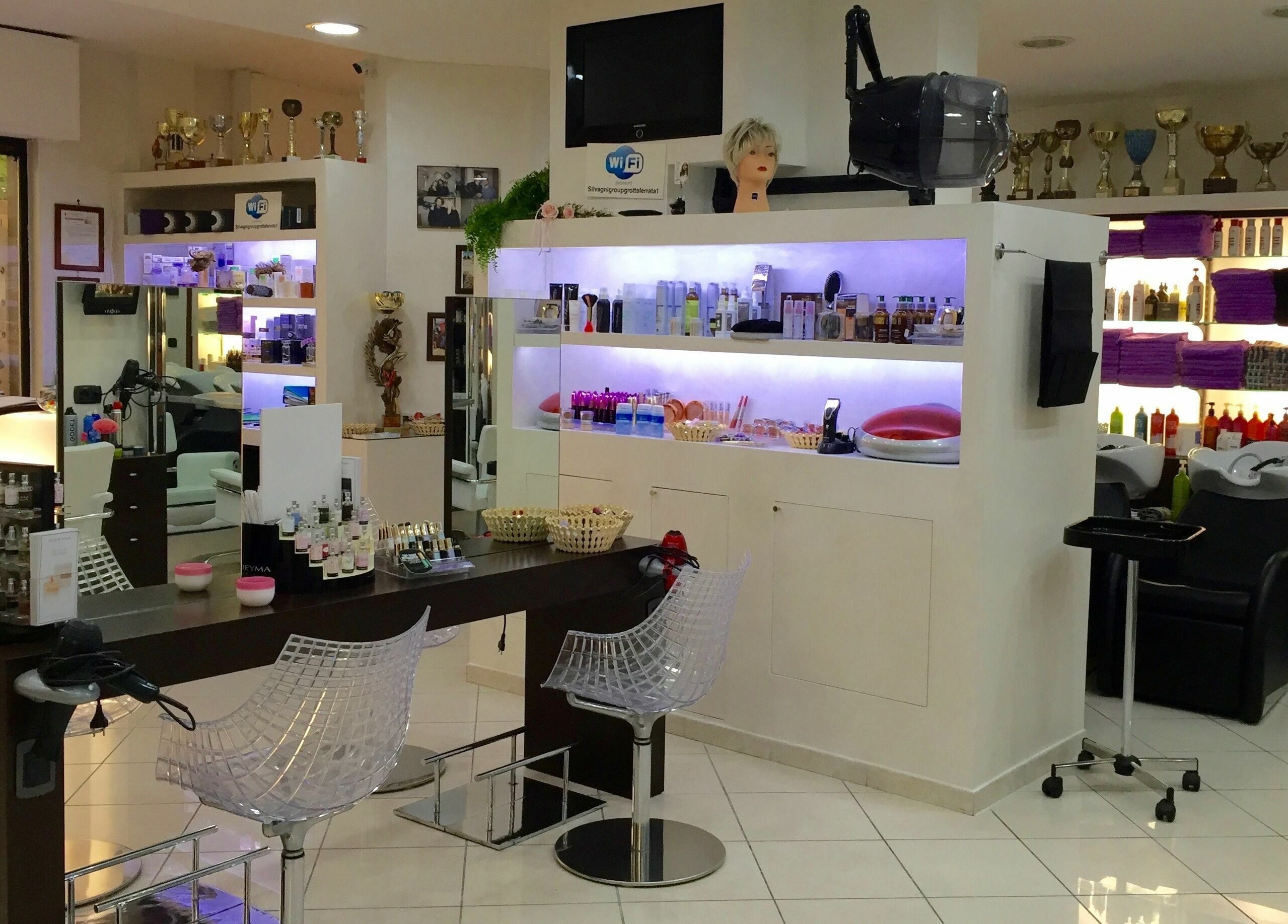 Interni moderni di Silvagni Group Parrucchieri a Grottaferrata, Lazio, IT, con sedie trasparenti e scaffali illuminati.