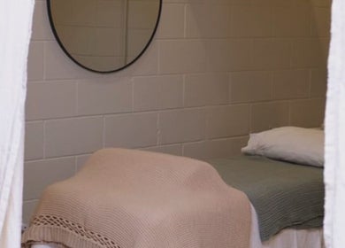 Cozy treatment room in yourSPAce, Christchurch, Canterbury Region, NZ, featuring a blanket-covered bed and round mirror.