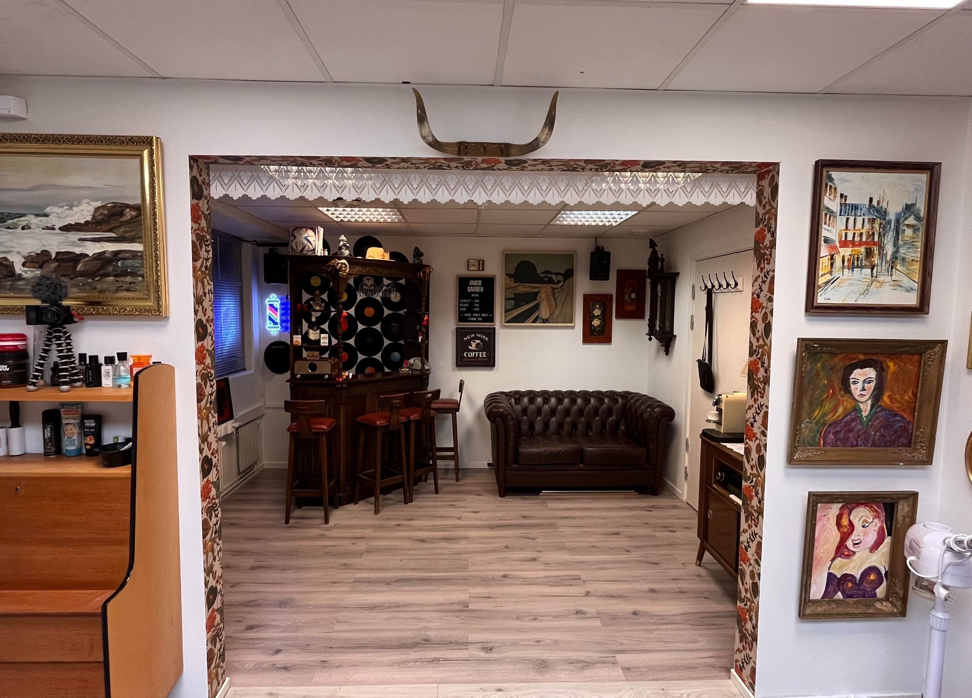 Stilig interiør hos JangoBarber i Oslo, Oslo, NO, med kunstverk på veggene og komfortabel sitteplass.