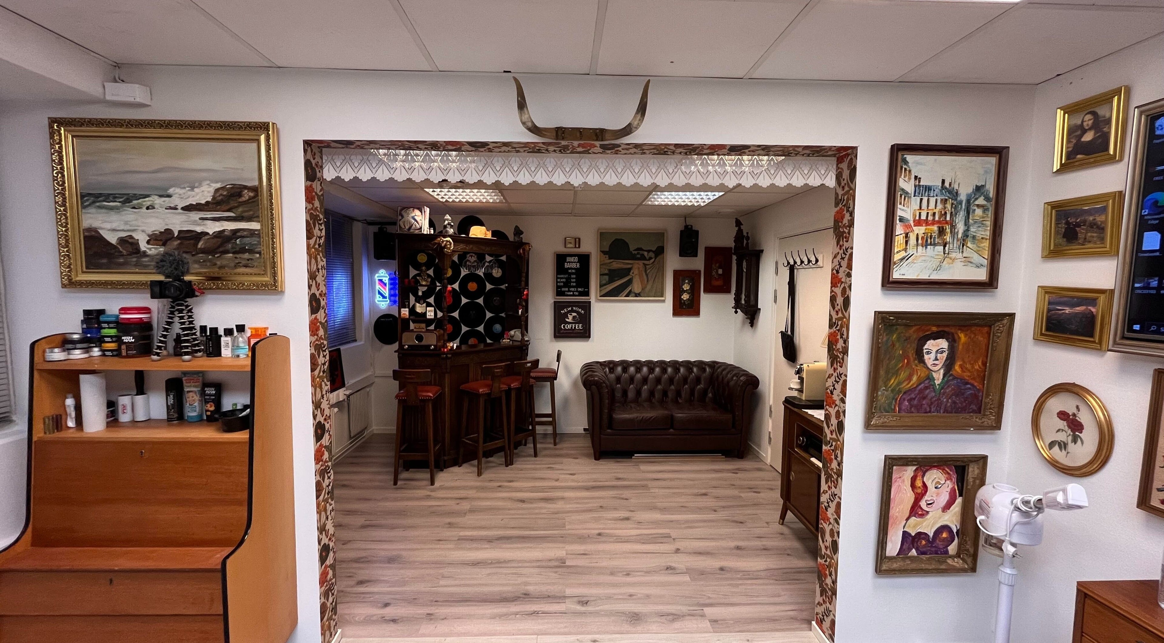 Stilig interiør hos JangoBarber i Oslo, Oslo, NO, med kunstverk på veggene og komfortabel sitteplass.