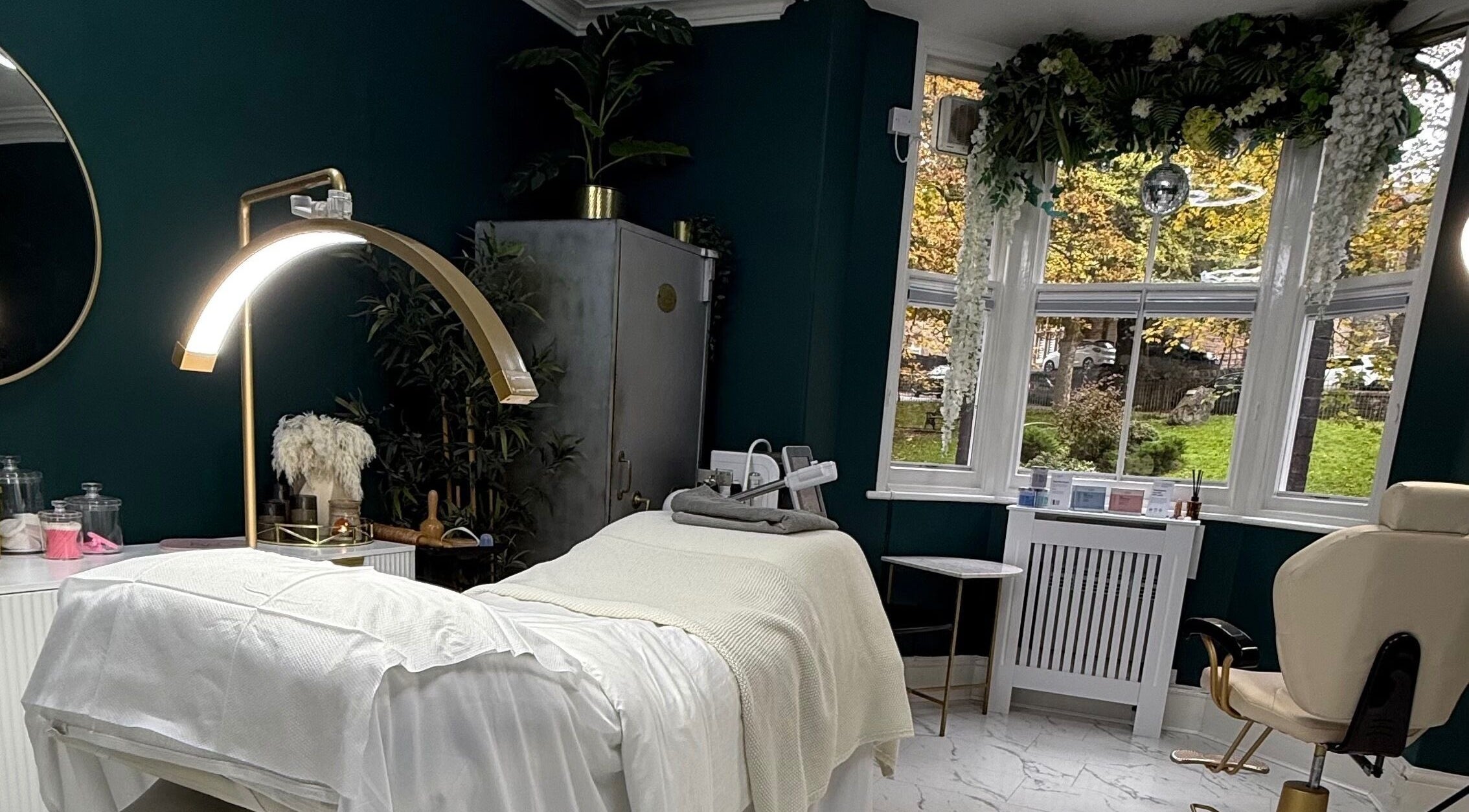 Elegant treatment room at Foxie Skin Clinic, Buxton, England, GB with a cozy spa bed and lush greenery.