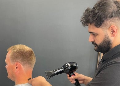 Kapper bij Ilyana Kapsalon Drachten Friesland, NL verzorgt herenkapsel met haardroger.