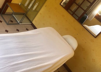 Sala de tratamiento en Cris Falcão Beauty PMU, Cambrils, Cataluña, ES, vista de cama con espejo y ventana.