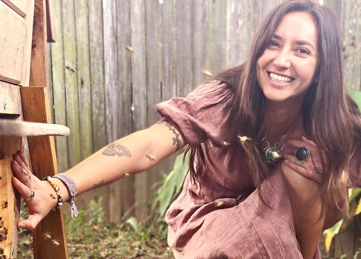 Smiling woman near beehive at Bee Alive, Mullumbimby, New South Wales, AU, showcasing natural beauty.