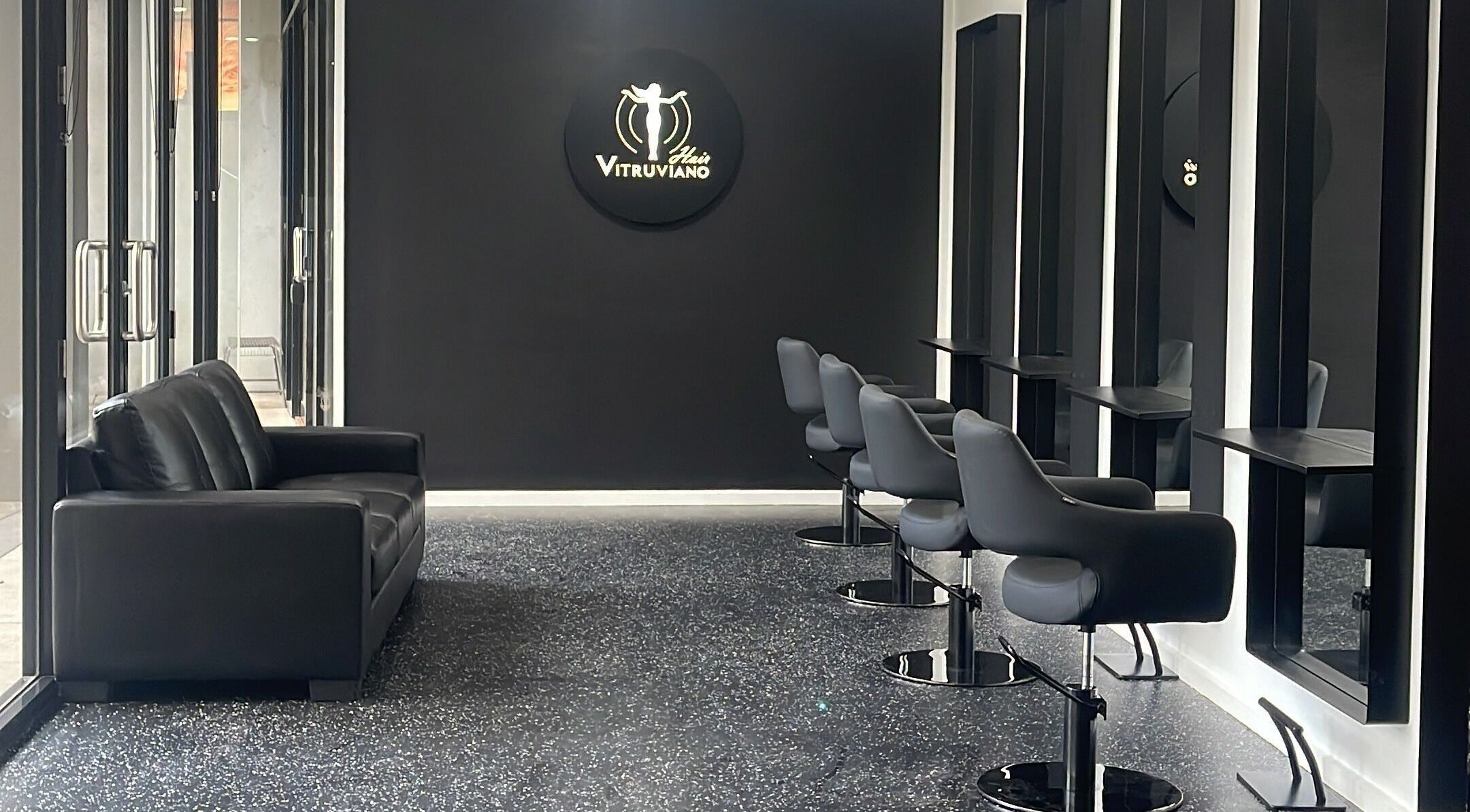 Interior of VITRUVIANO HAIR, Melbourne, Victoria. Modern black chairs and mirrors create a chic salon atmosphere.