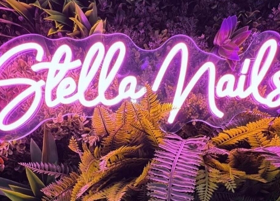 Enseigne néon 'Stella Nails' entourée de plantes à Bacilly, Normandie, FR, offrant ambiance chic et accueillante.