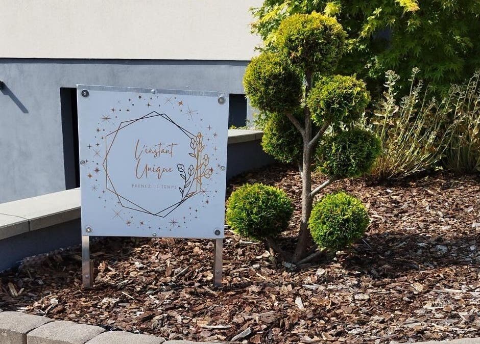 Panneau de L'instant Unique, situé à Gundershoffen, Grand Est, FR, entre des arbustes bien taillés.