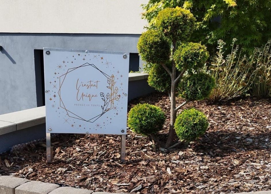 Panneau de L'instant Unique, situé à Gundershoffen, Grand Est, FR, entre des arbustes bien taillés.