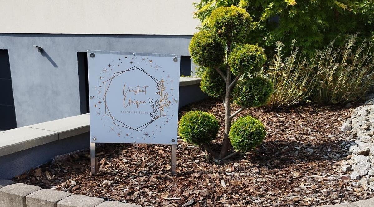 Panneau de L'instant Unique, situé à Gundershoffen, Grand Est, FR, entre des arbustes bien taillés.