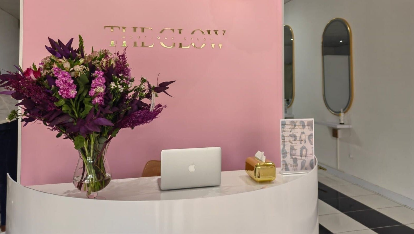 Reception desk at The Glow Boutique Salon in Hillcrest, Kwazulu-natal, ZA with vibrant flowers and a laptop.