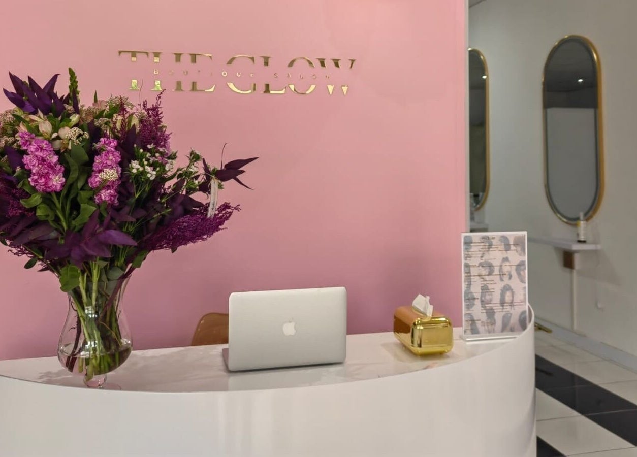 Reception desk at The Glow Boutique Salon in Hillcrest, Kwazulu-natal, ZA with vibrant flowers and a laptop.