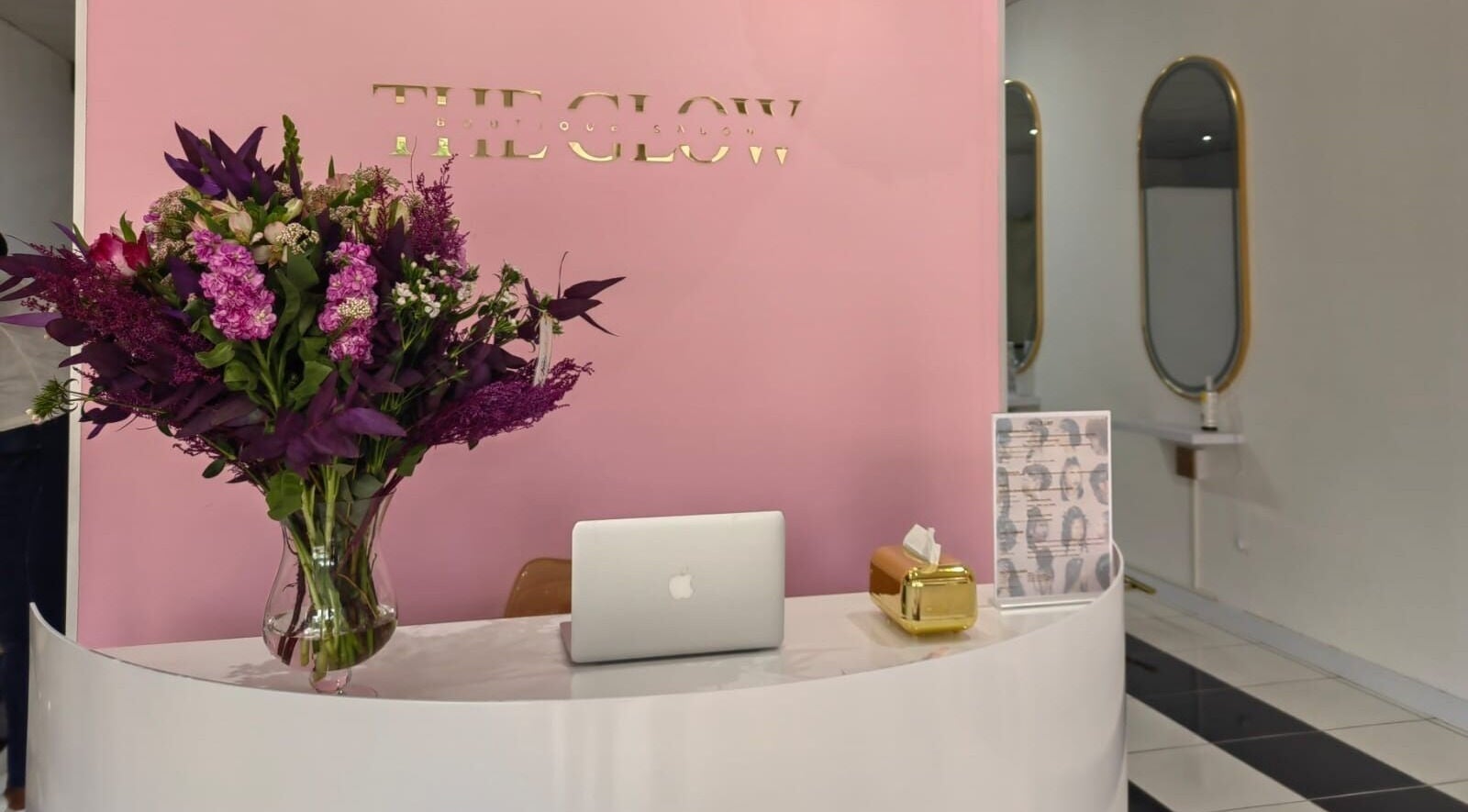 Reception desk at The Glow Boutique Salon in Hillcrest, Kwazulu-natal, ZA with vibrant flowers and a laptop.
