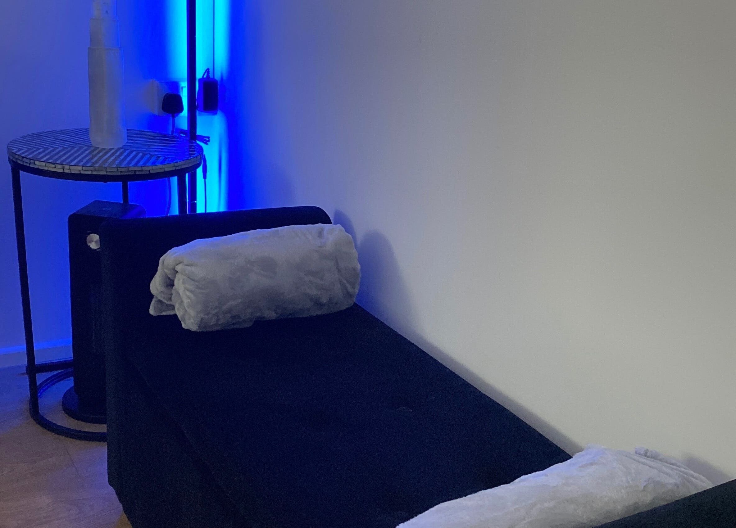Cozy treatment bed at Sculpted By Ariella, Cheltenham, England, GB with calming blue lighting.