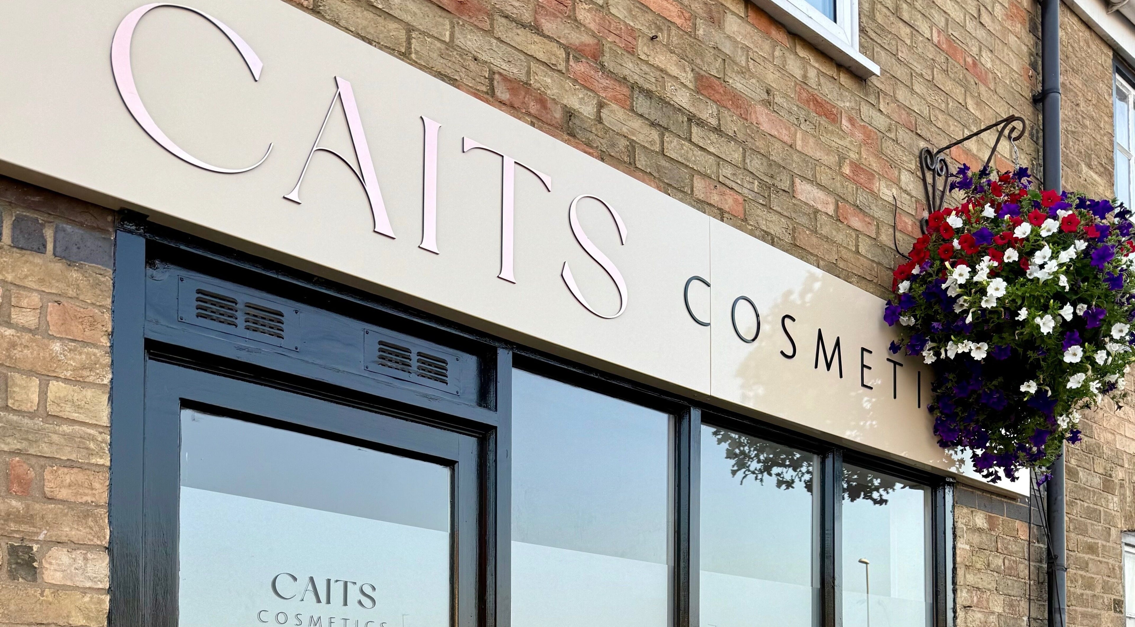 Front of Caits Cosmetics, Whittlesey, England, GB with elegant signage and hanging floral decor.