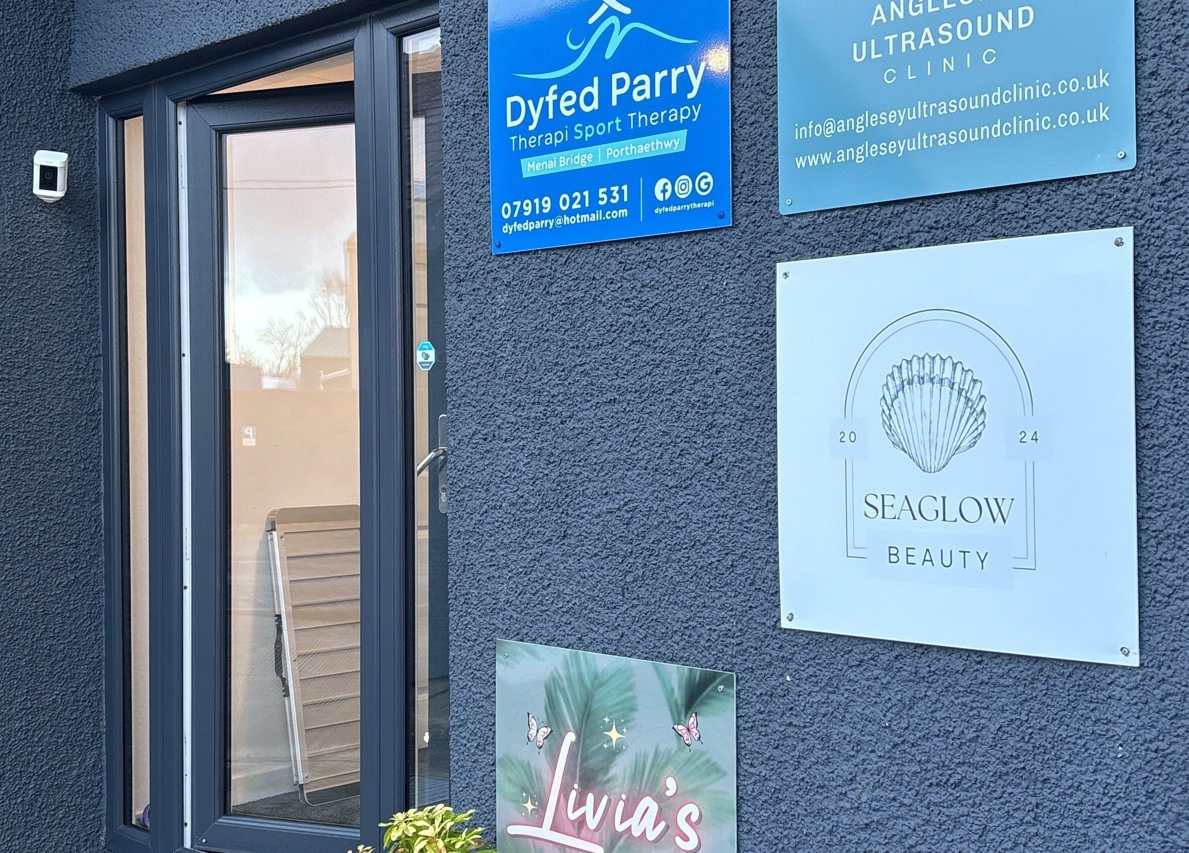 Entrance of Seaglow Beauty at Menai Bridge, Wales, GB, featuring signs and a modern glass door.