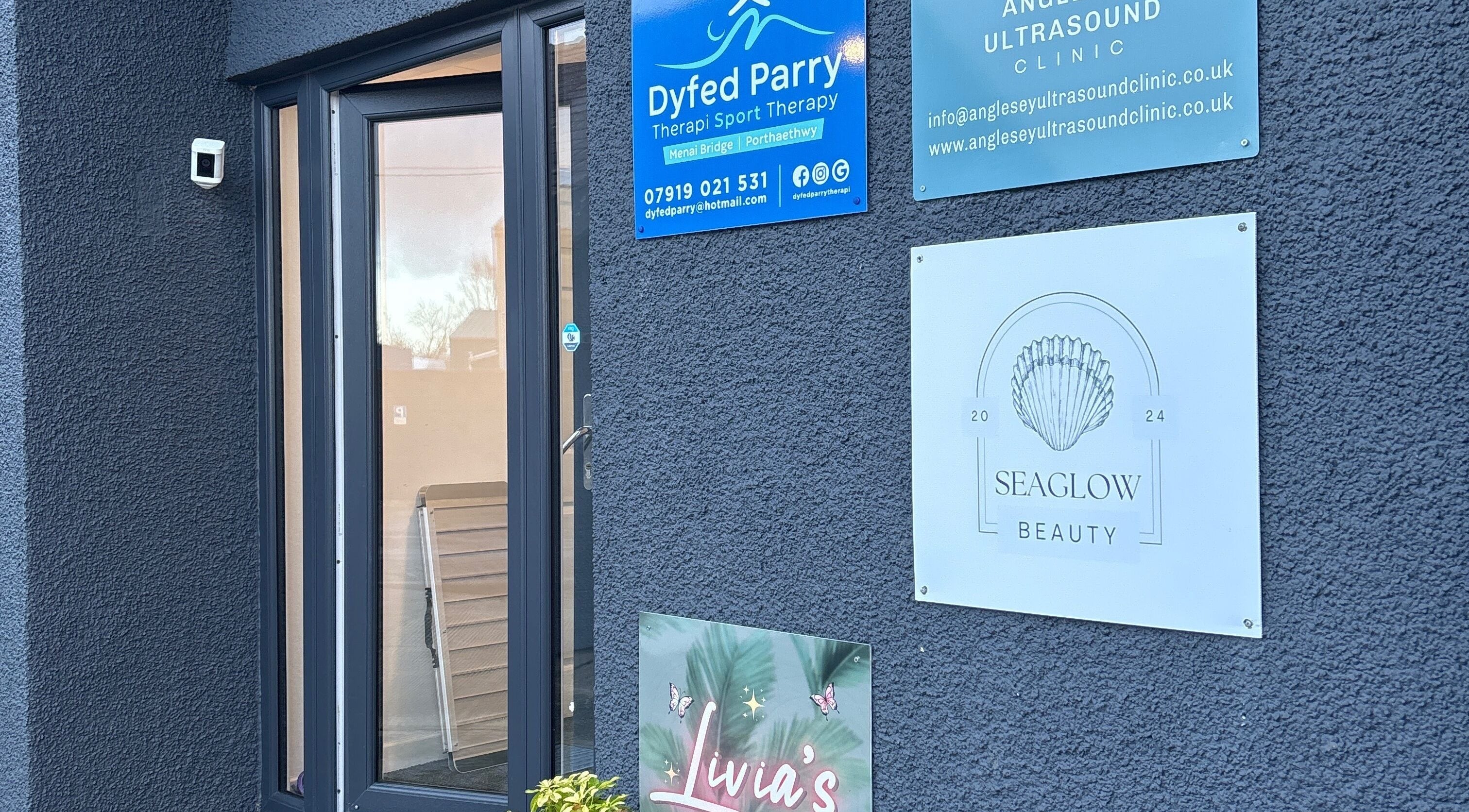 Entrance of Seaglow Beauty at Menai Bridge, Wales, GB, featuring signs and a modern glass door.