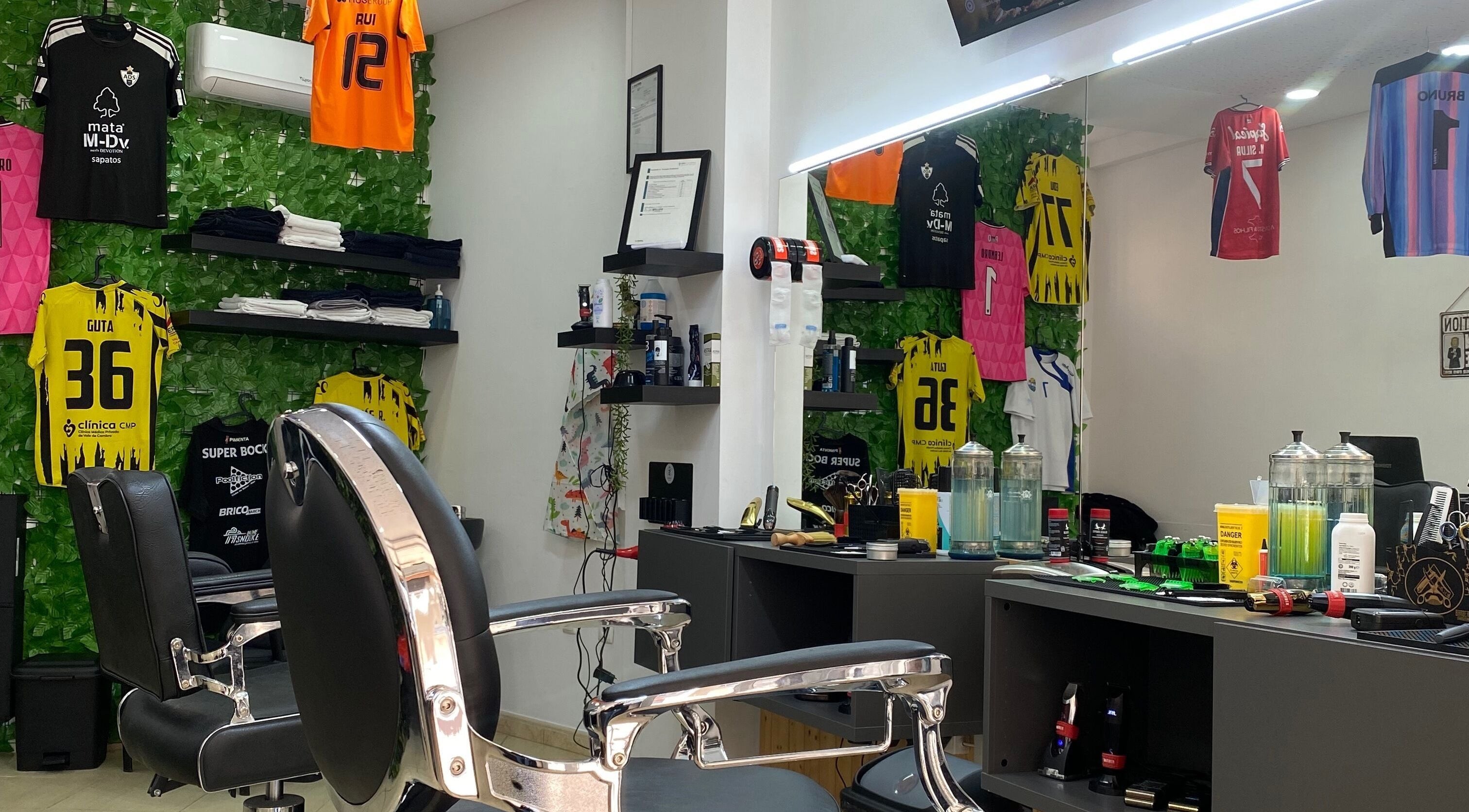 Interior moderno da Rkbarbershop em Vale De Cambra, Aveiro, PT com cadeiras de barbeiro e camisolas desportivas.