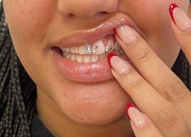 Close-up of jeweled teeth and red tipped nails at Laterals and Lashes, Coventry, England, GB.