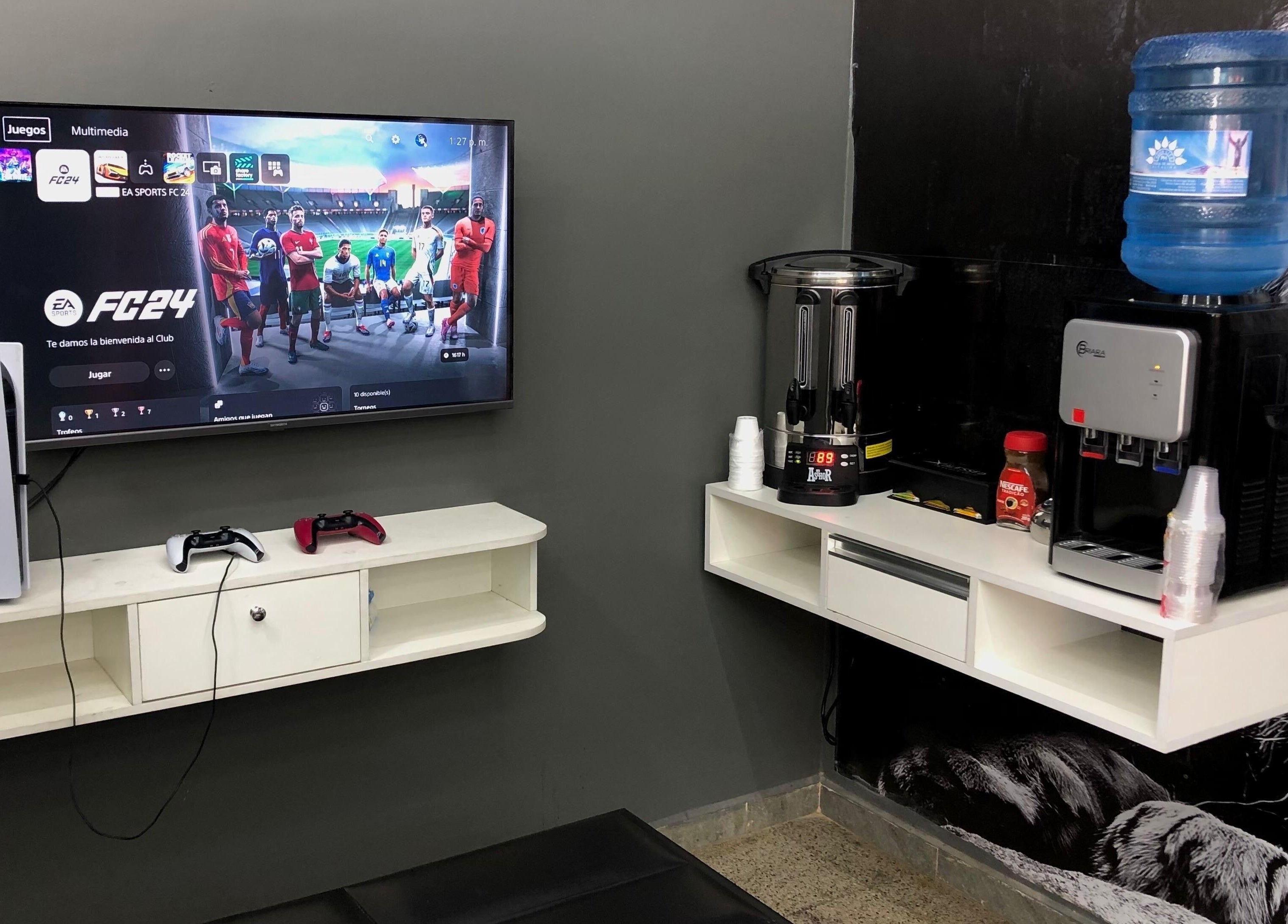Sala de juegos en Blessed Barber Club Santos Doumont, 7mo Anillo, Santa Cruz, con consola PS5 y estación de bebidas.