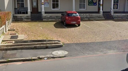 Entrance of Wellue Beauty in Paarl, Western Cape, ZA, featuring a red car in a peaceful parking area.
