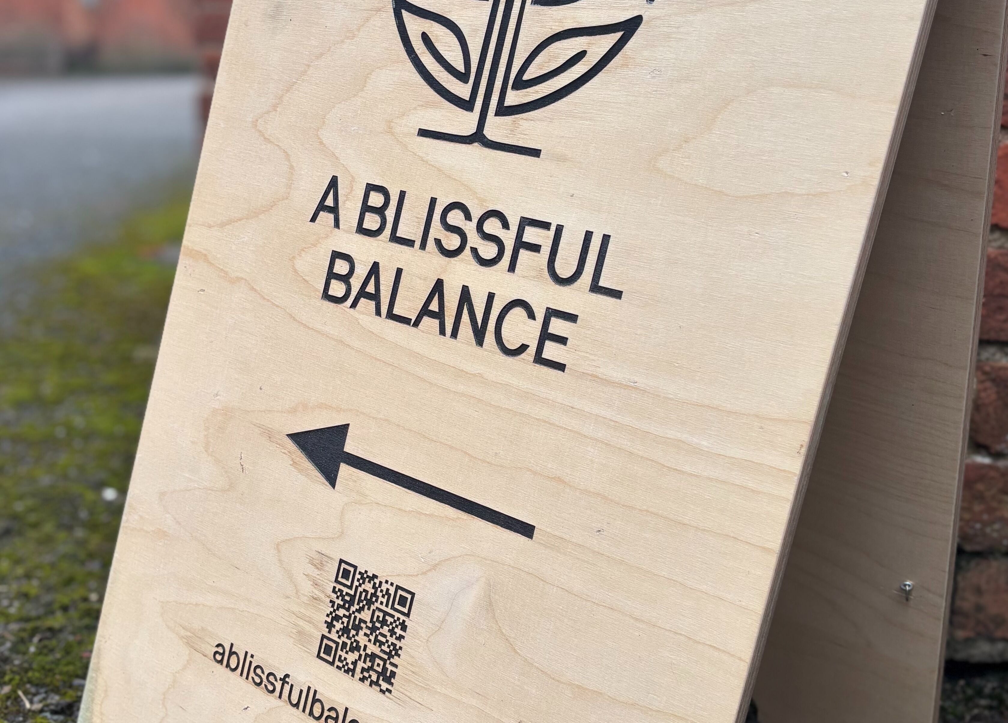 Wooden signboard of A Blissful Balance, Wellesbourne, England, GB directing to wellness center.