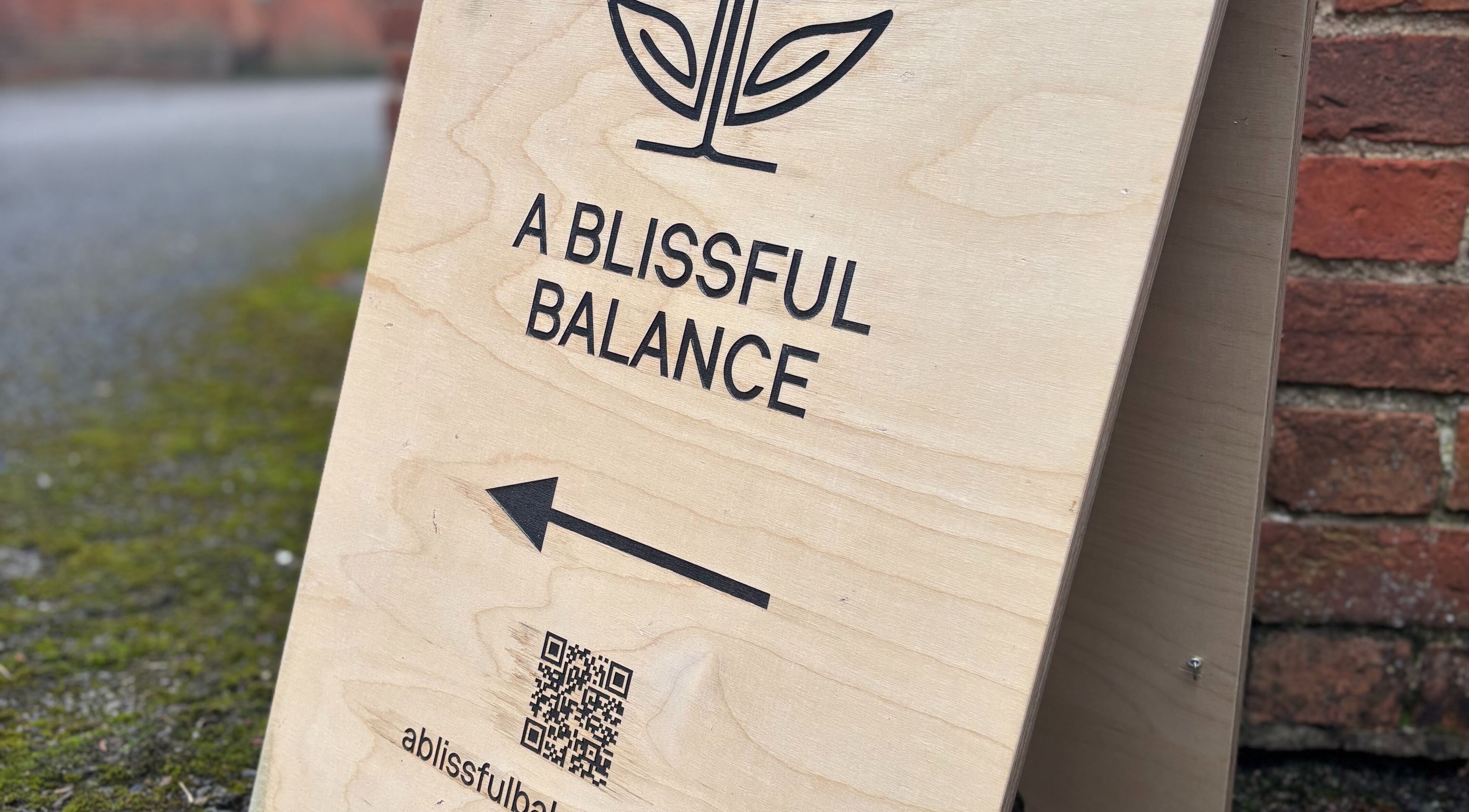 Wooden signboard of A Blissful Balance, Wellesbourne, England, GB directing to wellness center.