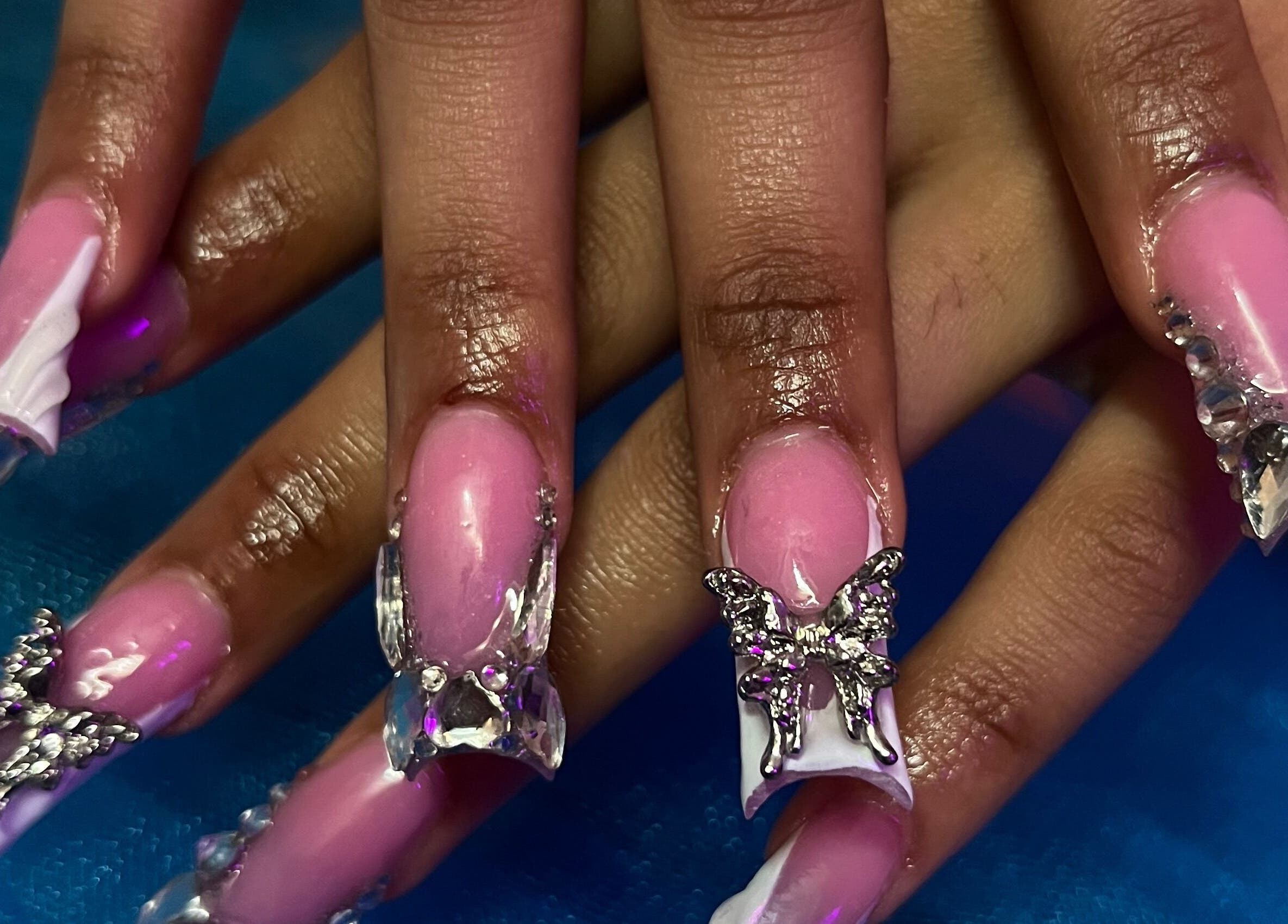 Elegant butterfly nail art at Visage VERITAS in Troy, New York, US features pink polish and crystal accents.