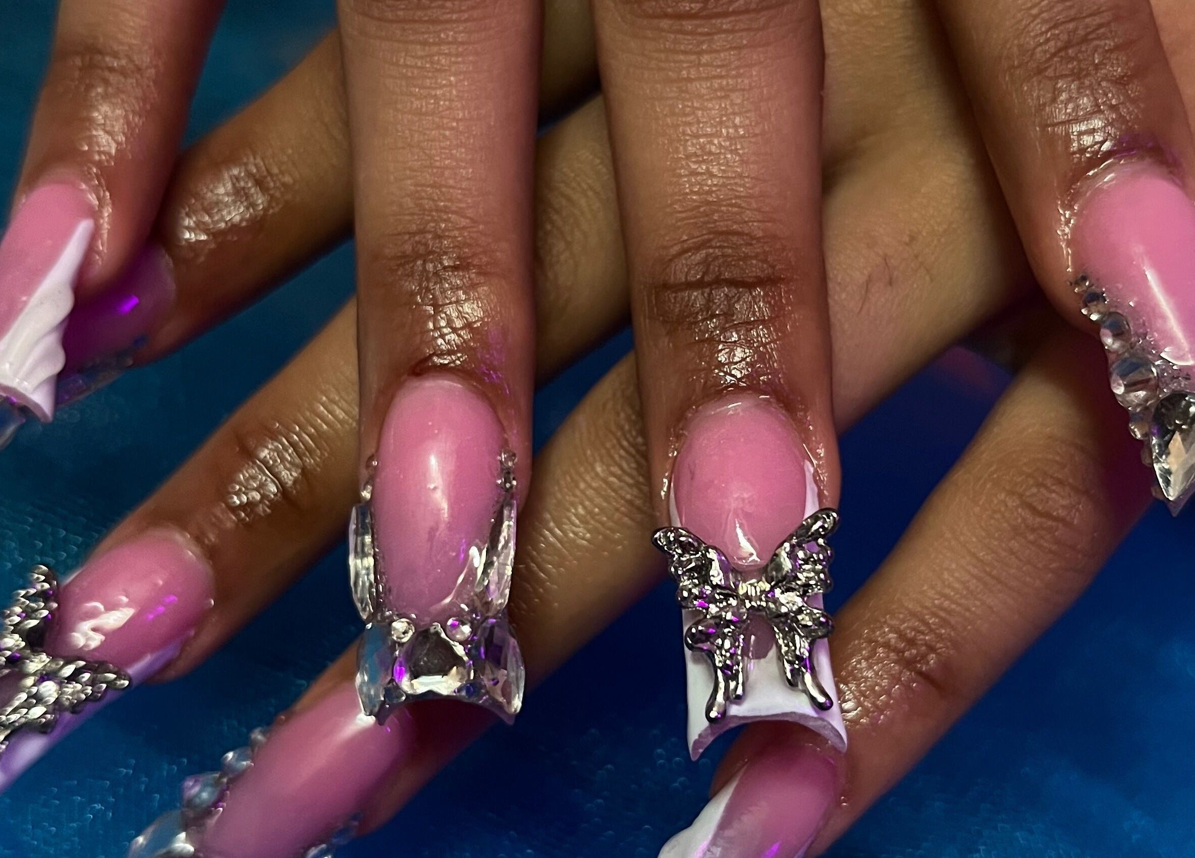 Elegant butterfly nail art at Visage VERITAS in Troy, New York, US features pink polish and crystal accents.